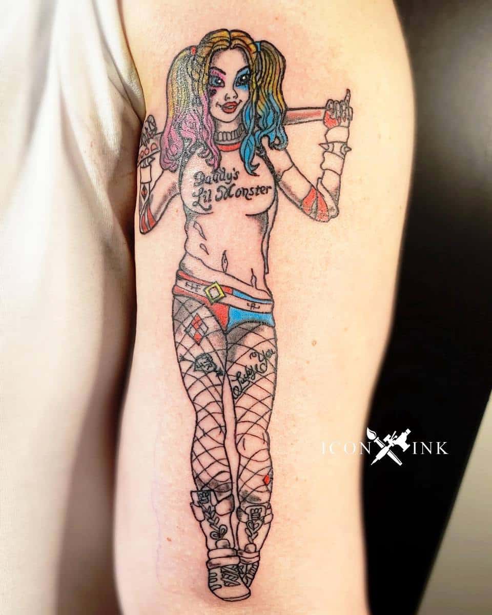 Tattoo of Harley Quinn in her 'Daddy's Lil Monster' outfit with fishnet stockings and holding a bat, done in a colorful, pin-up style on the upper arm