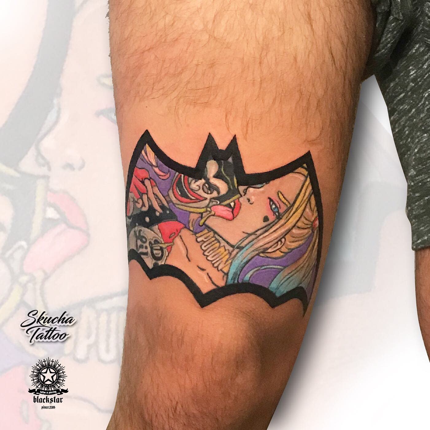 A tattoo of Harley Quinn and Joker inside a bat emblem on an upper arm