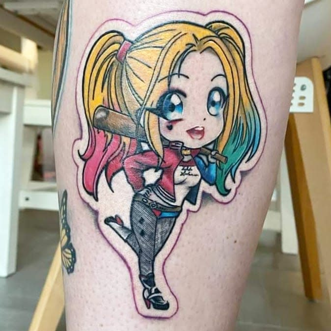 Tattoo of Harley Quinn with colorful hair holding a weapon on skin with other tattoos