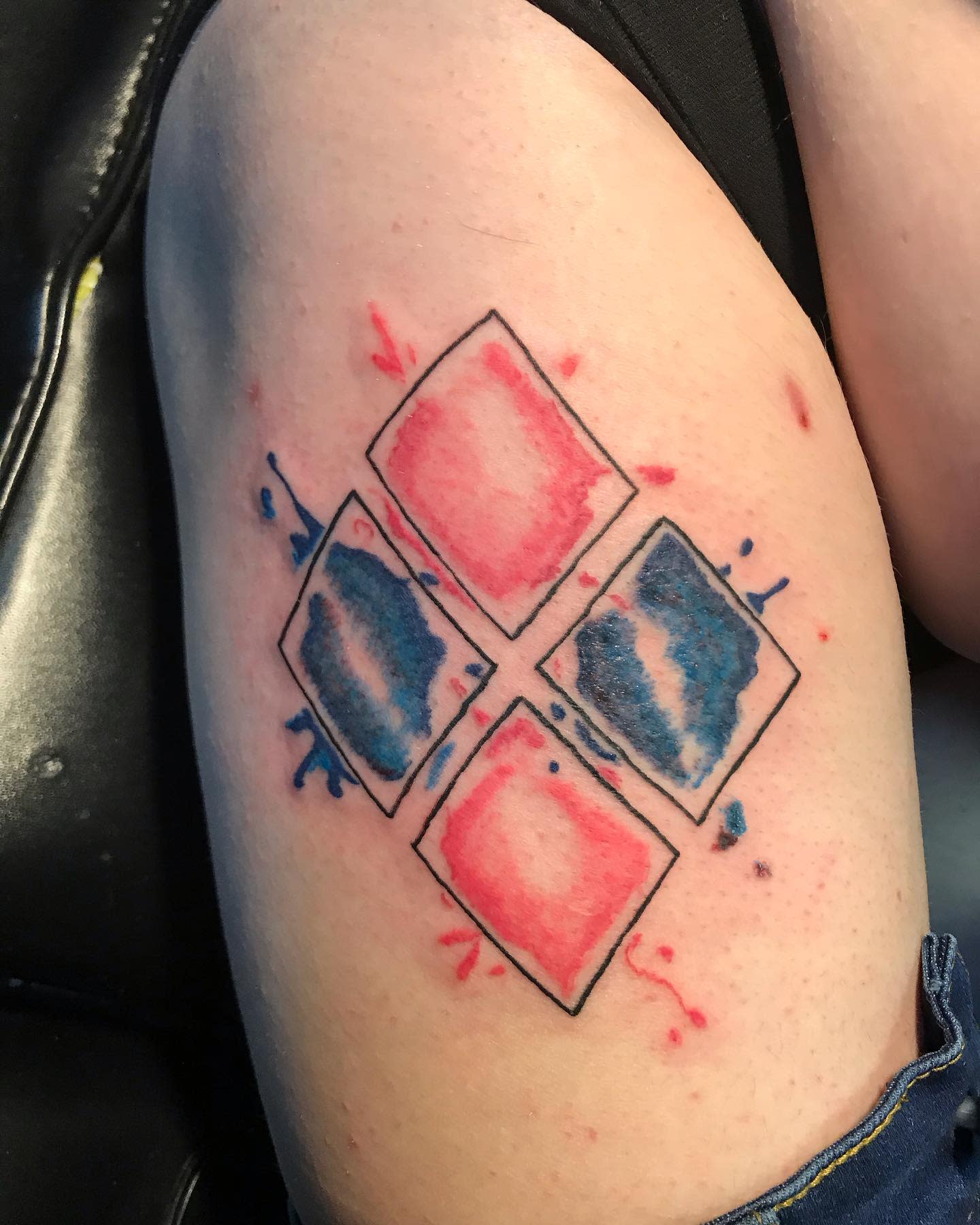 Tattoo of four diamonds in two colors on skin, two red and two blue, with paint splatter effect