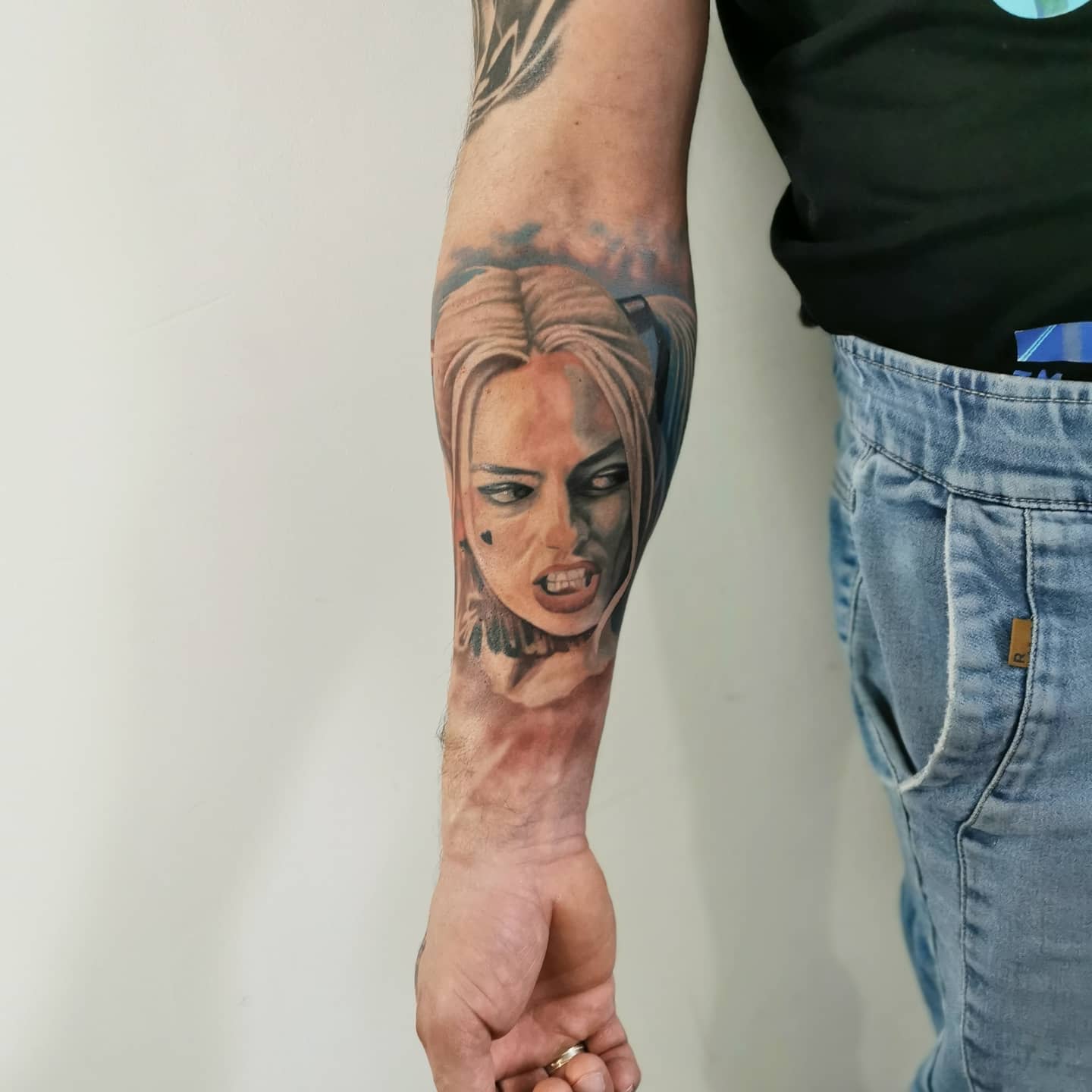 Realistic forearm tattoo of Harley Quinn with an intense expression, showing her teeth