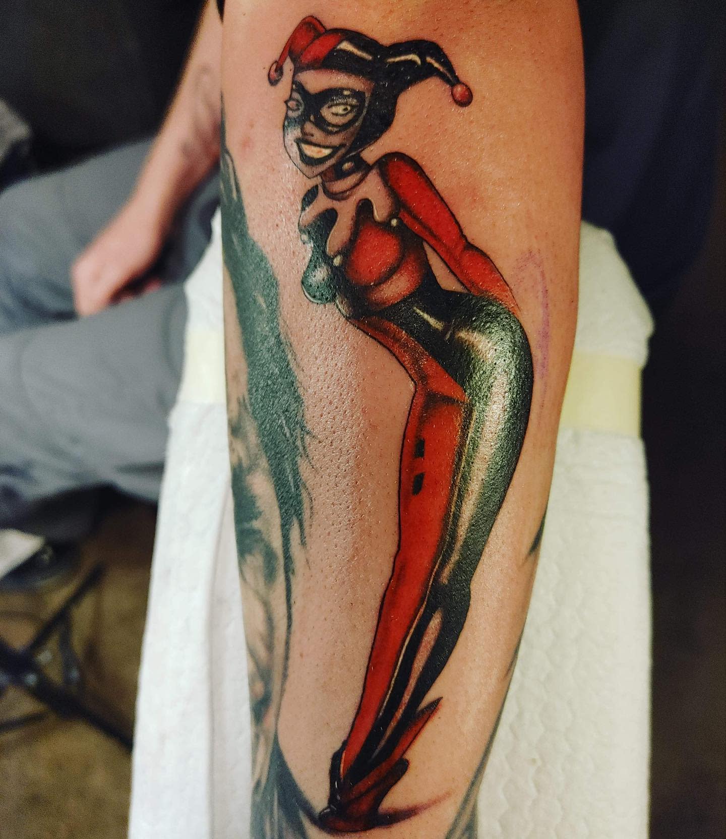 Tattoo of Harley Quinn in her classic jester outfit from the Batman animated series on the upper arm
