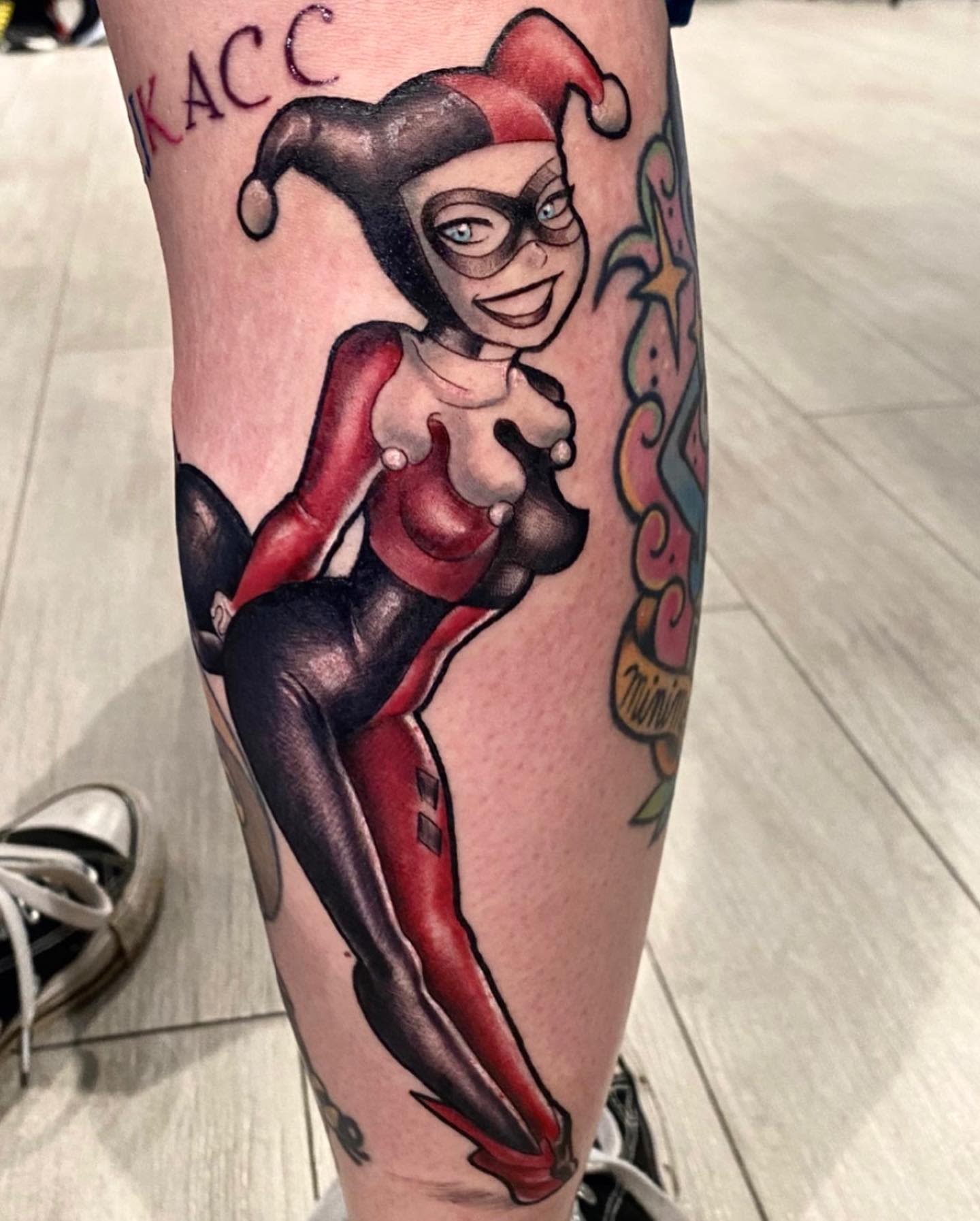 Tattoo of Harley Quinn in her classic red and black jester outfit with a playful pose on the calf