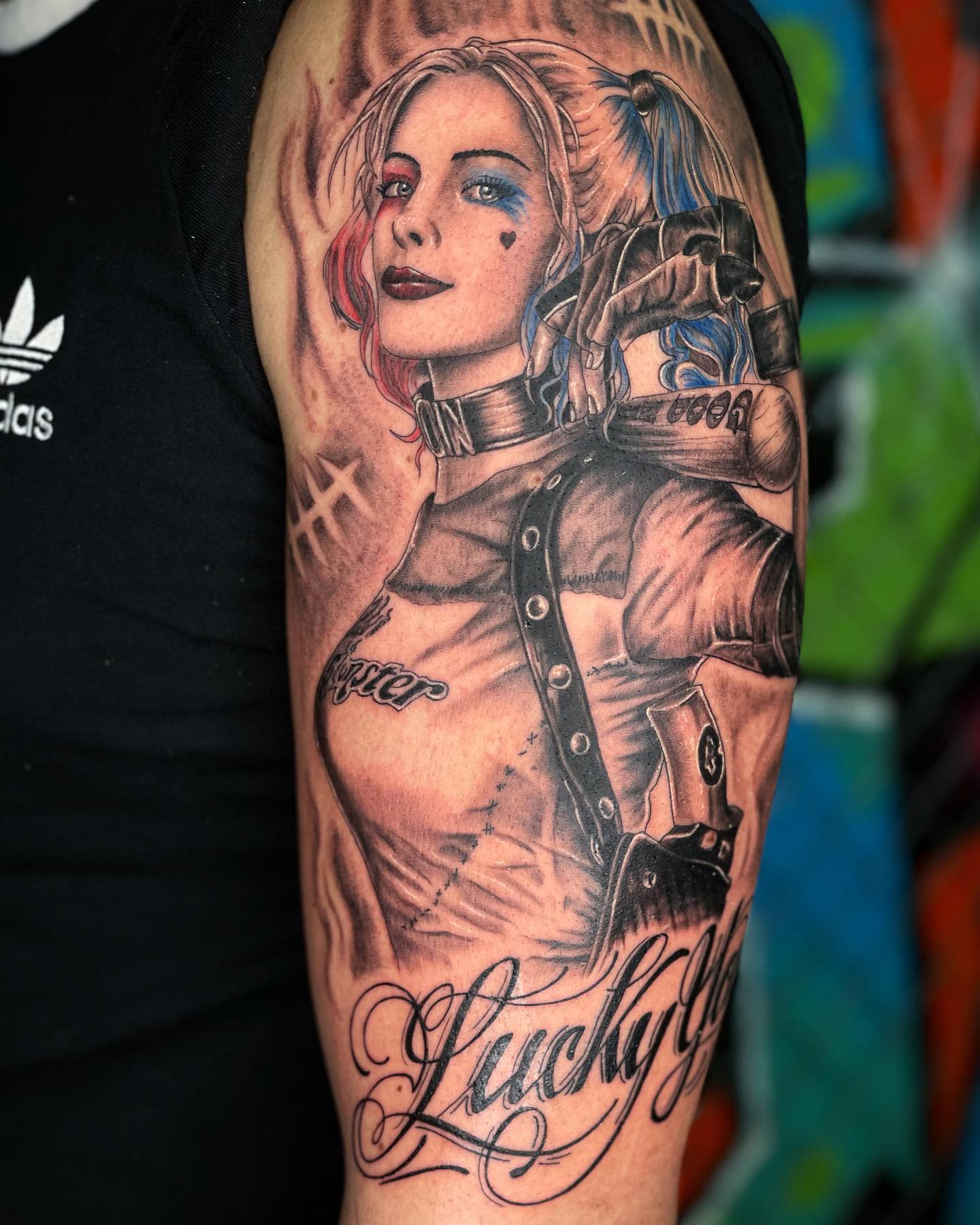 Realistic tattoo of Harley Quinn with red and blue pigtails, holding a baseball bat on the upper arm, with 'Lucky' in script below
