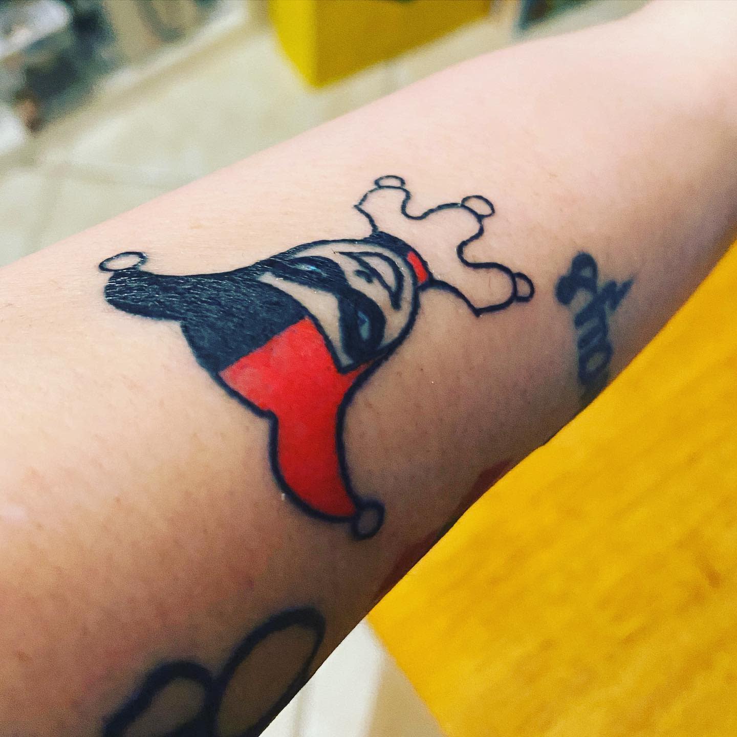 Small minimalist tattoo of Harley Quinn's face in her jester hat on the forearm