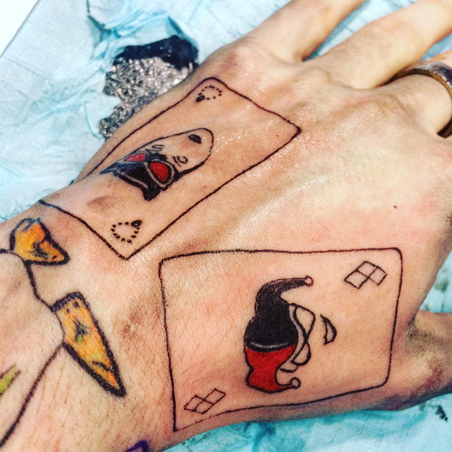Tattoo of two small playing cards on the hand, each featuring Harley Quinn's jester hat and face