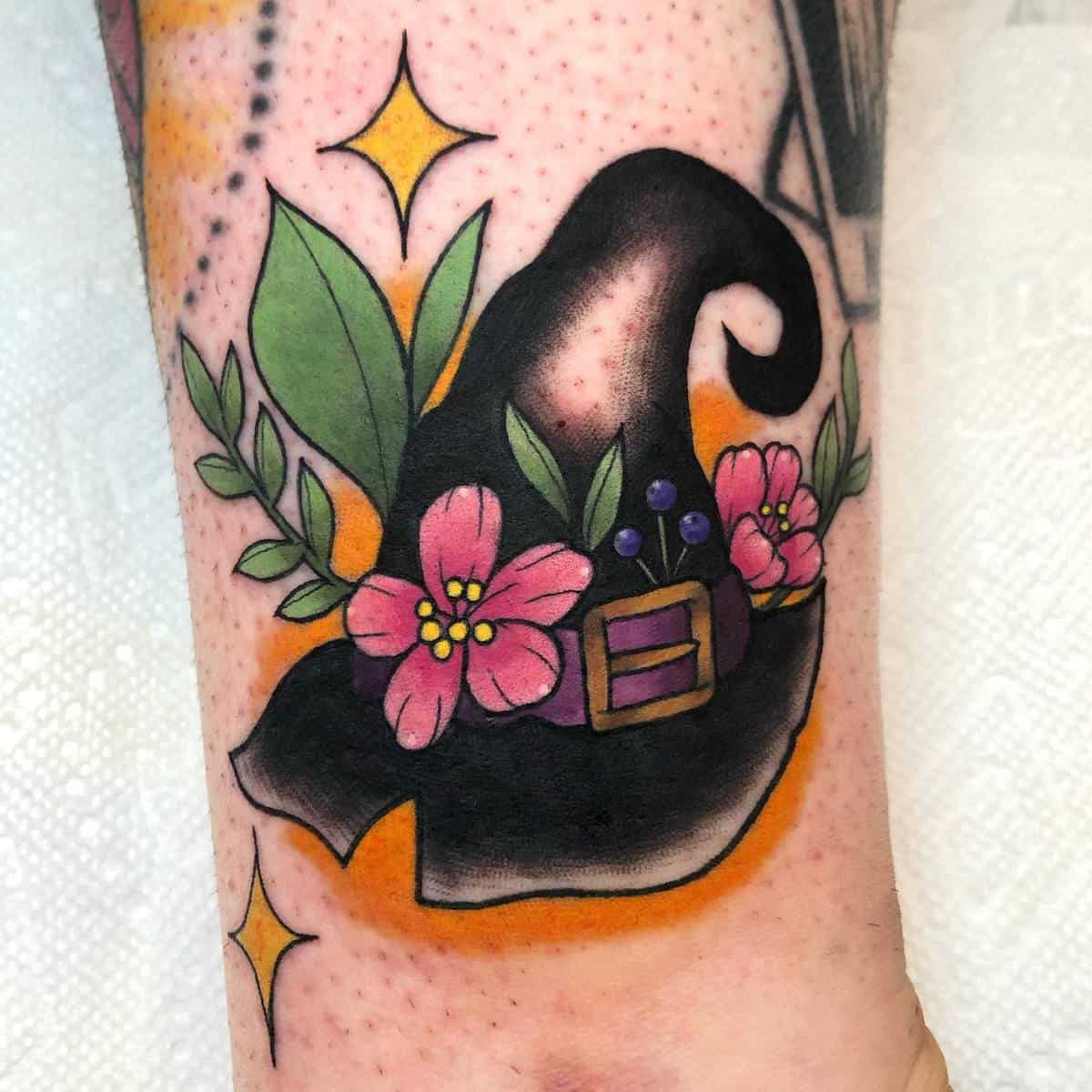 Tattoo of a witch hat adorned with pink flowers and leaves