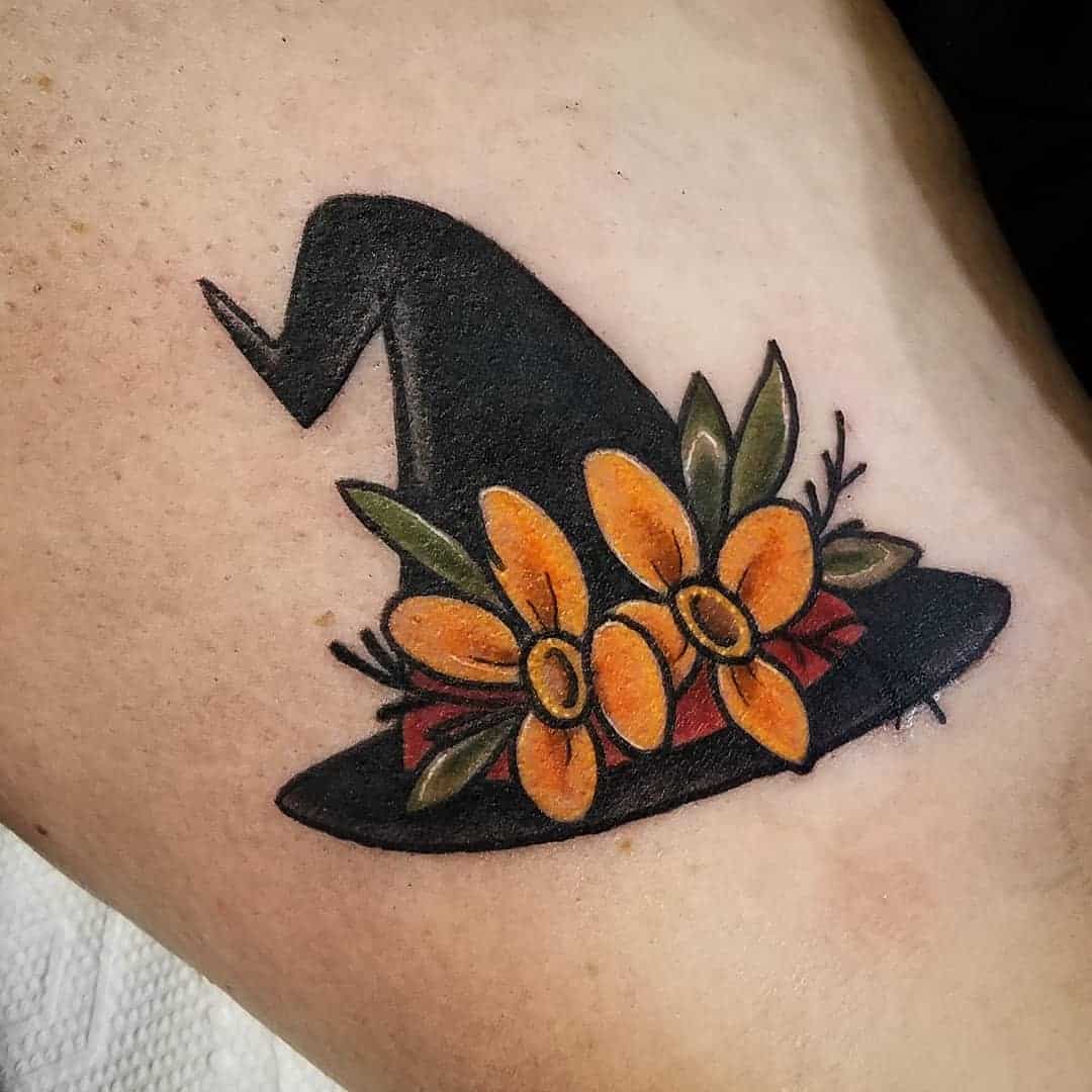 Tattoo of a witch hat adorned with yellow flowers and green leaves on skin