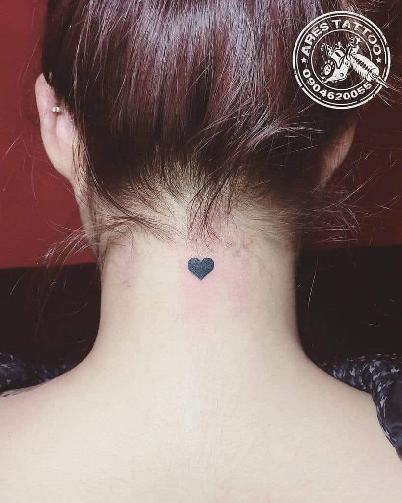 A small black heart tattoo at the back of the neck