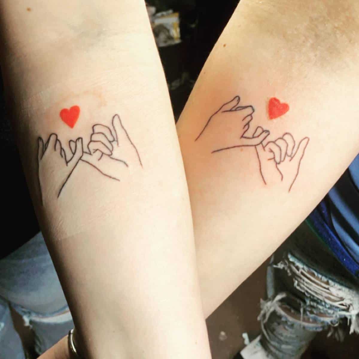 Two arms with matching tattoos of pinky promises and red hearts above them