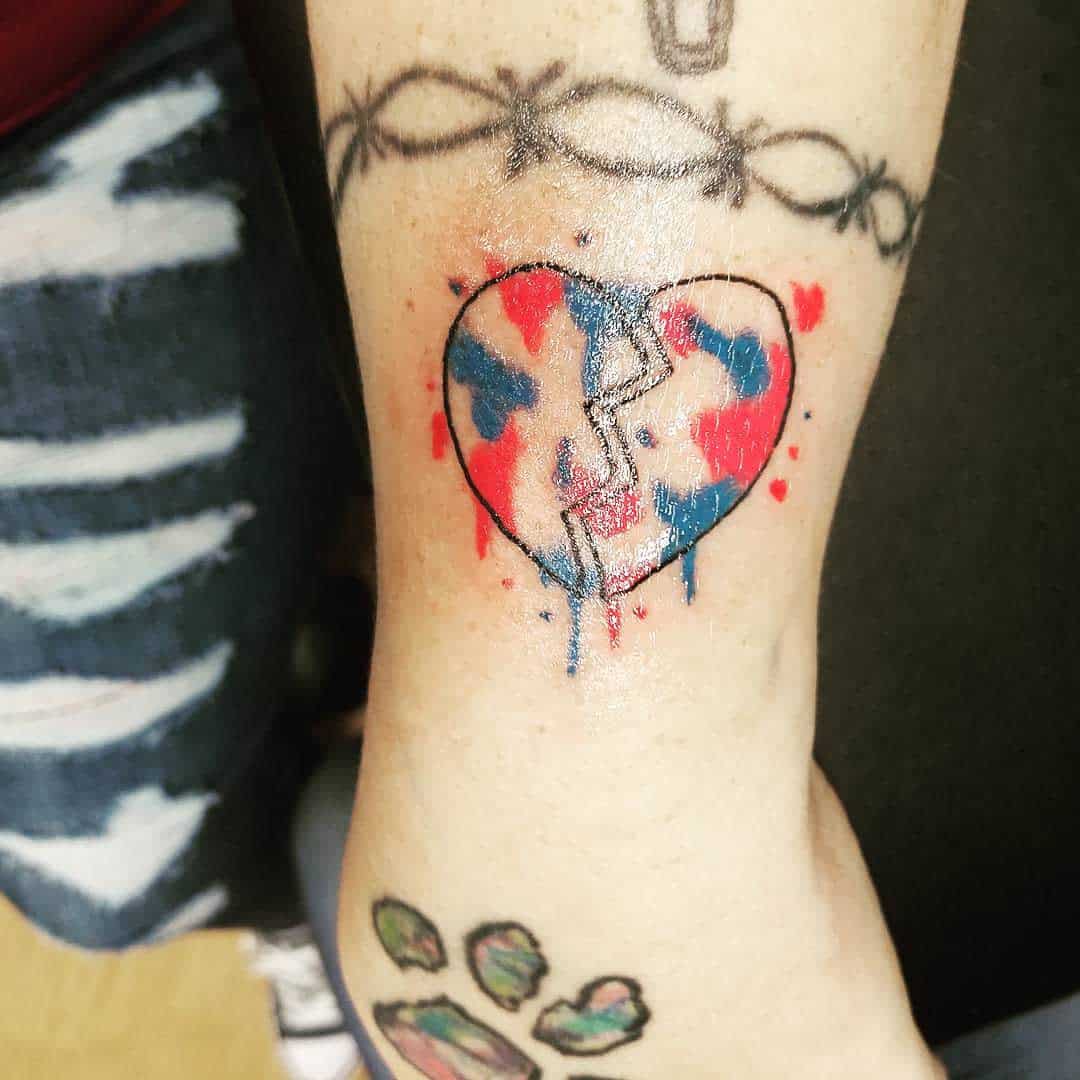 Tattoo of a cracked heart with red and blue colors, placed on inner arm near barbed wire and paw print tattoos