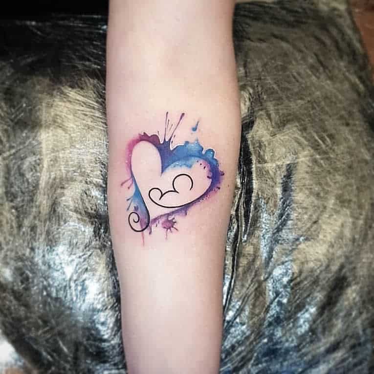 Arm tattoo: a colorful heart with blue and pink splash effects and a black swirl design in the center