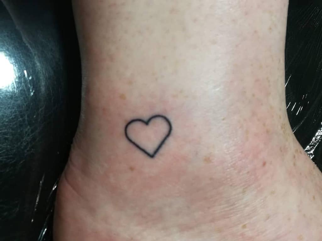 A small, simple heart tattooed on the inner side of an ankle
