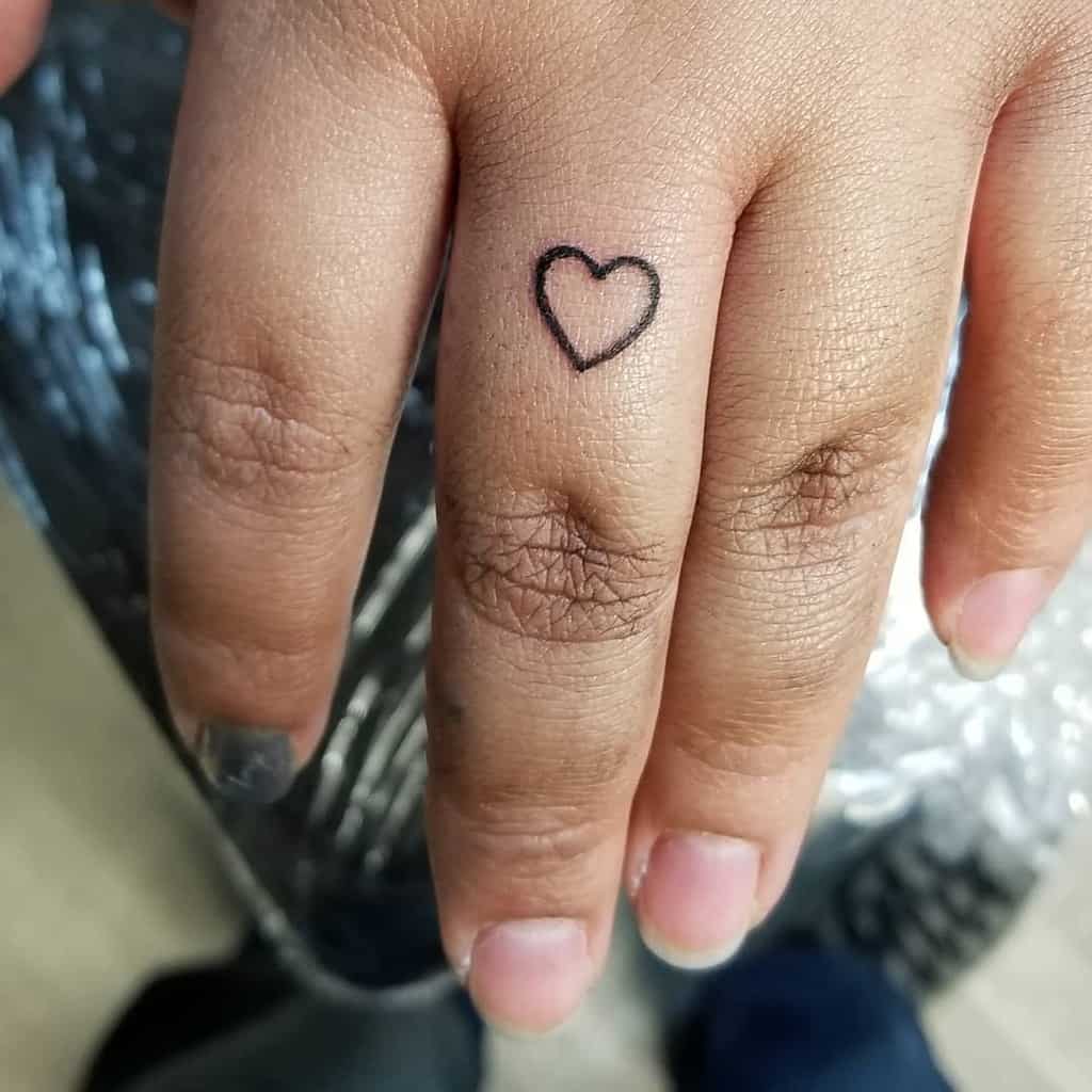 A simple heart tattoo is inked on the ring finger of a hand