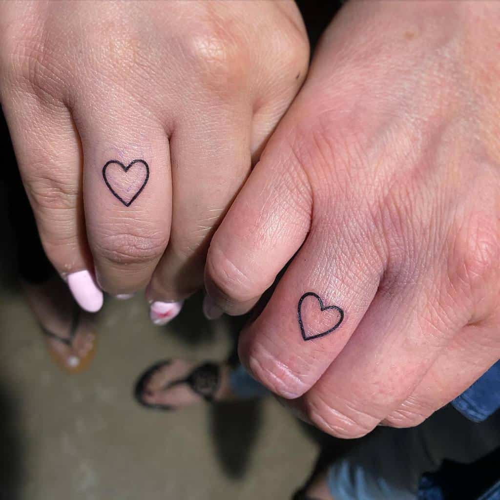 Two hands with matching heart outline tattoos on their ring fingers