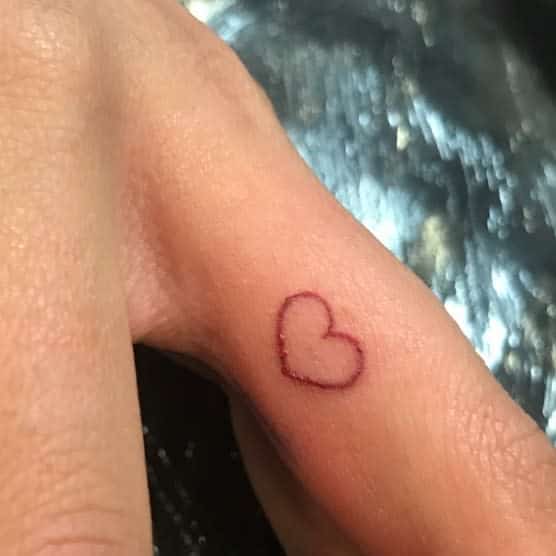 A simple heart outline tattoo on the side of a finger