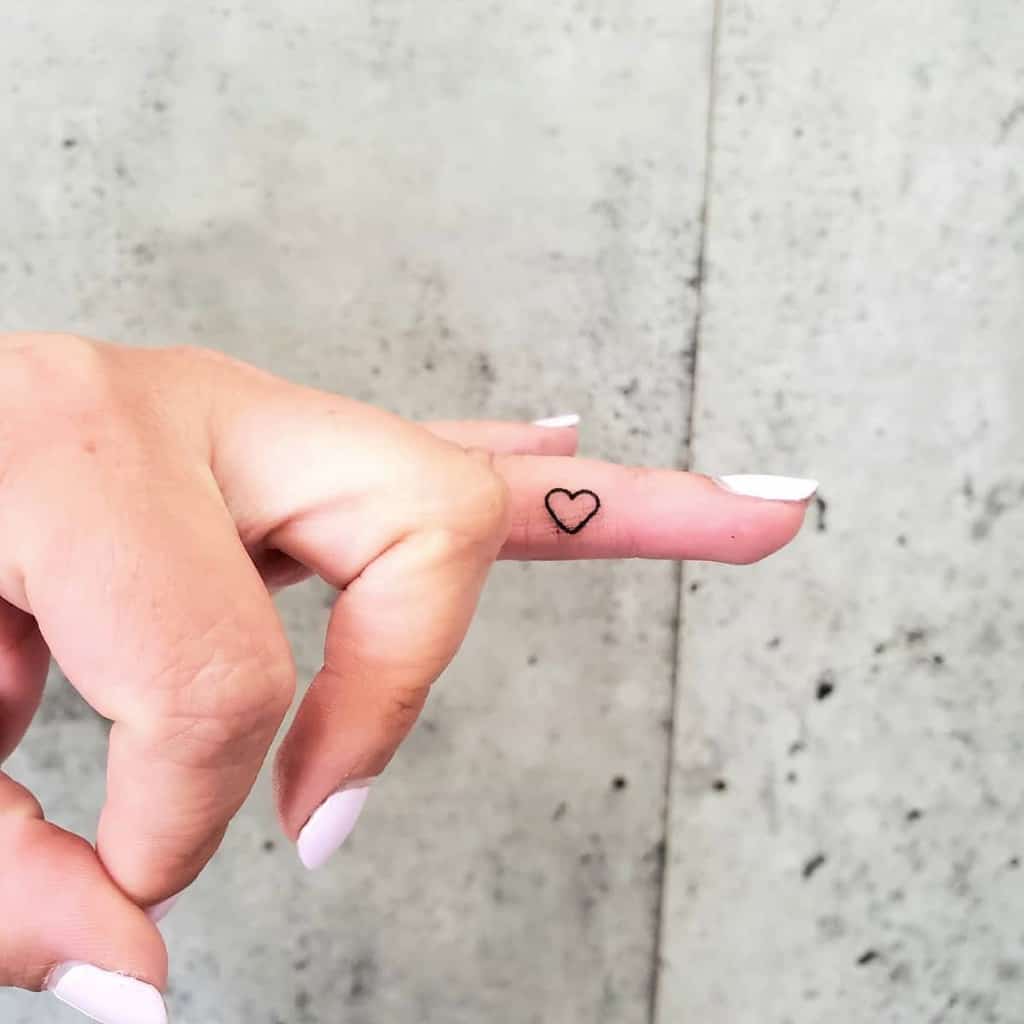 A tiny, outlined heart tattoo on the side of a finger