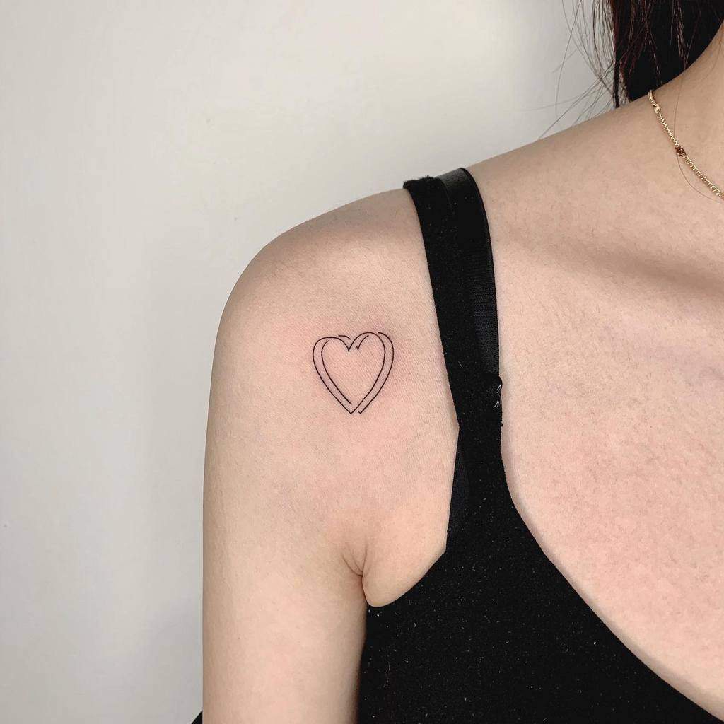 A simple heart tattoo outline on a person's upper shoulder near the collarbone