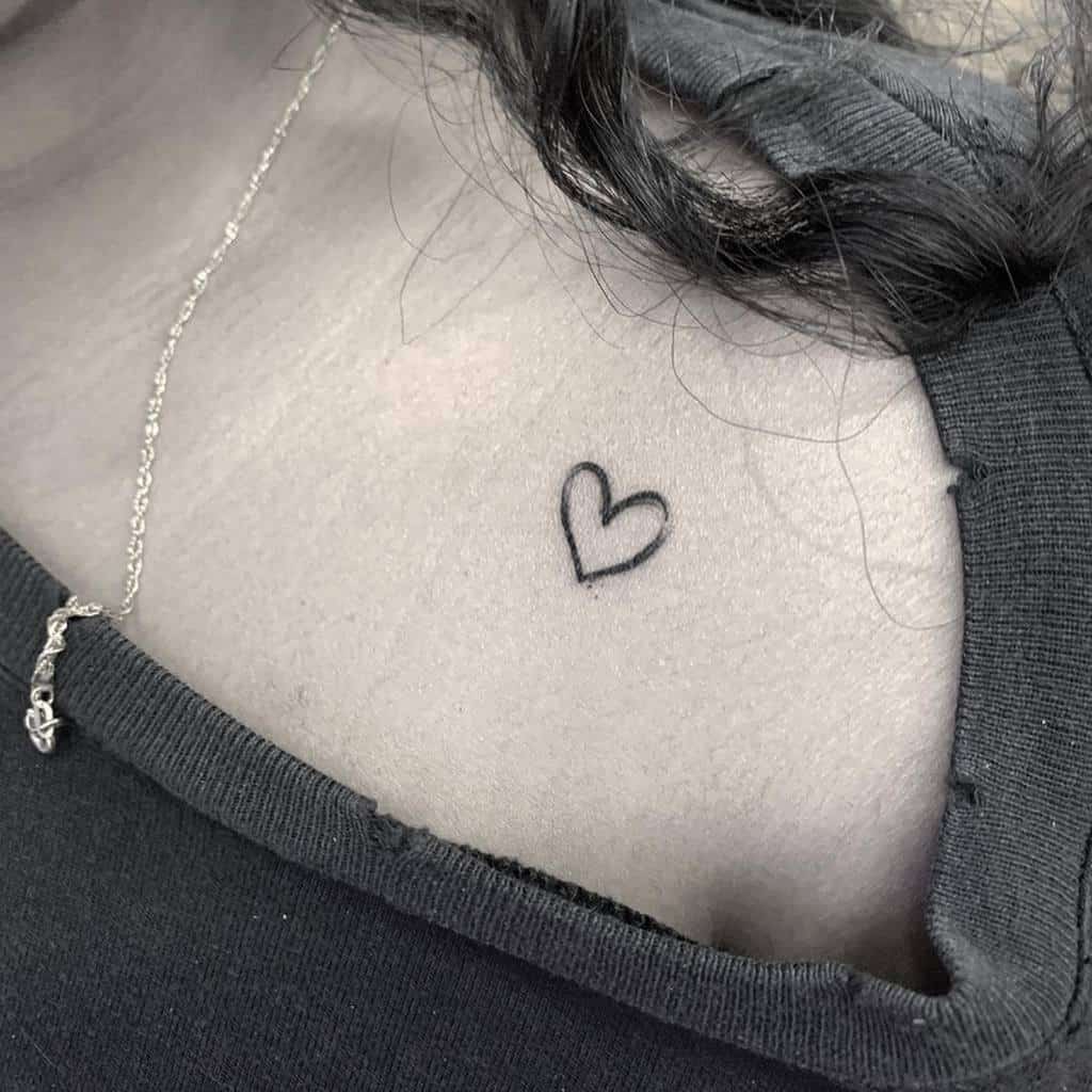 A small heart tattoo near a person's collarbone