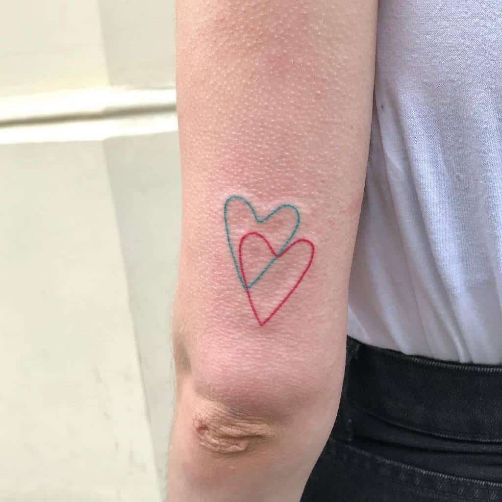 A tattoo with overlapping blue and red hearts on an arm above the elbow