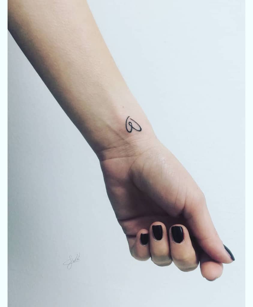 A wrist with a small black heart tattoo