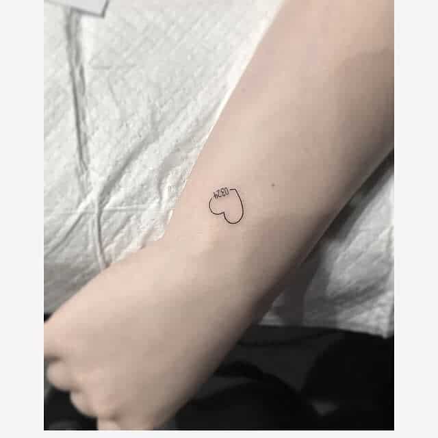 A small heart tattoo with "0324" inside it on a person's forearm