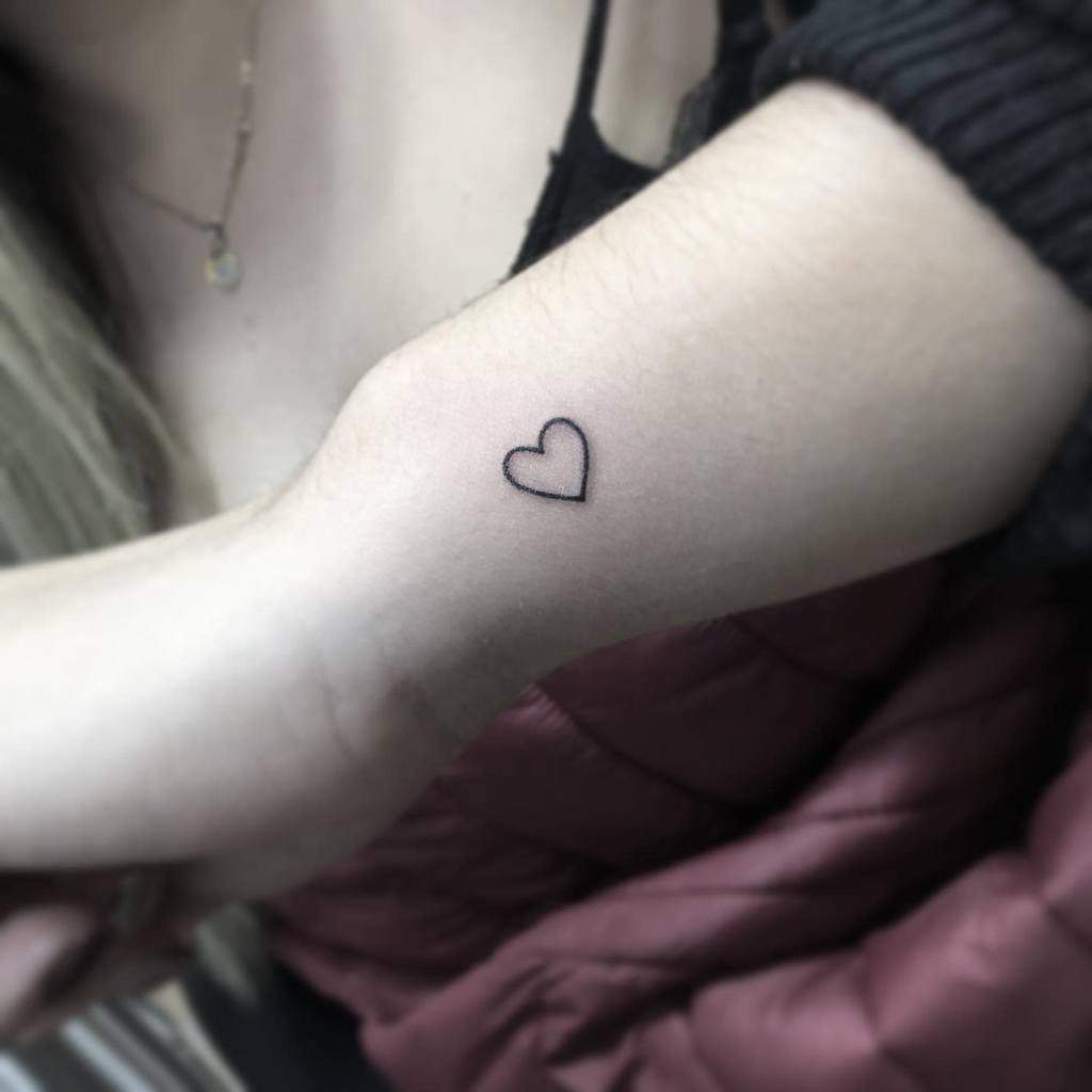 Tiny heart outline tattoo on a person's forearm near the wrist