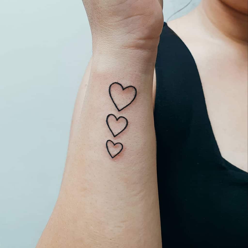 Three black outlined heart tattoos on a person's forearm, ascending in size from wrist to elbow