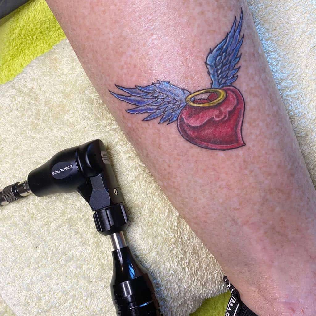 Tattoo of a vibrant red heart with angel wings on a leg