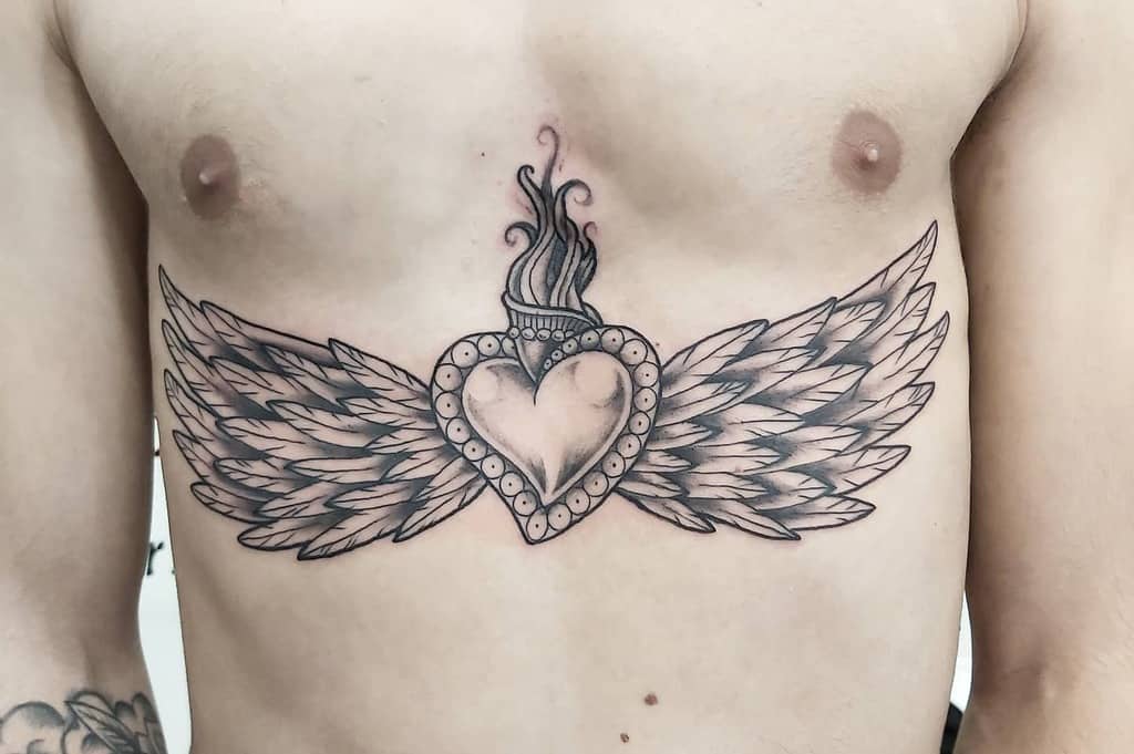 Tattoo of a heart with angel wings and flames on a person's chest