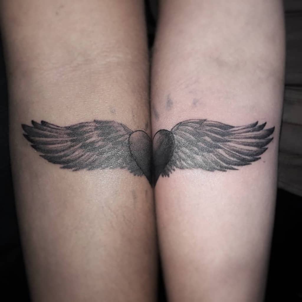 Close-up of a tattoo depicting angel wings gracefully forming a heart on two arms pressed together