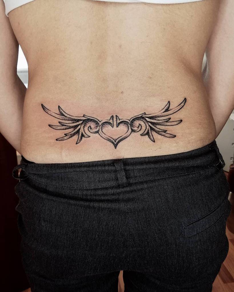 Lower back tattoo featuring a striking tribal heart design with intricate wings