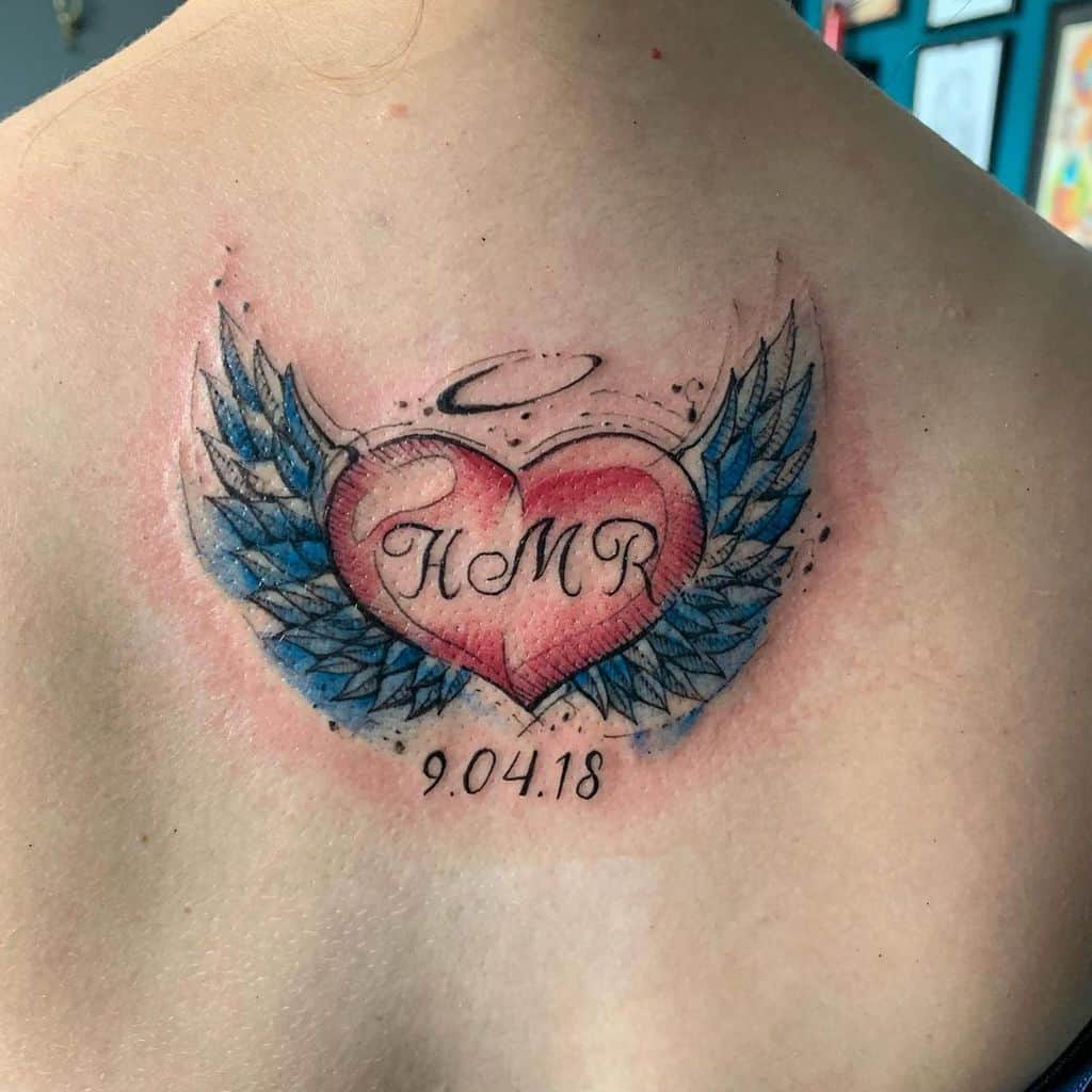 Colorful tattoo featuring a heart with angel wings and a halo, with the initials 'HMR' and a date '9.04.18'