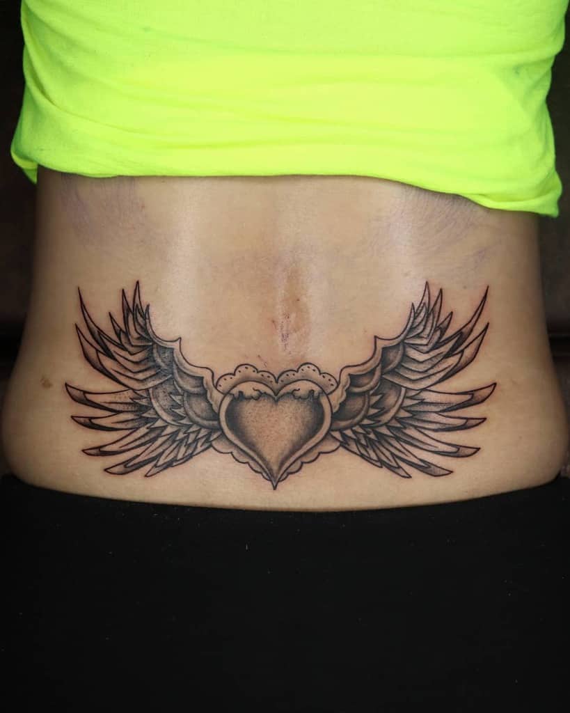 A tattoo showcasing a heart entwined with wings graces the person's lower back
