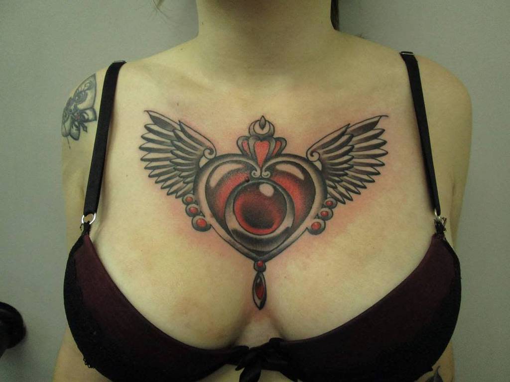 Woman with a large heart tattoo on her chest, adorned with intricate wings, wearing a black bra