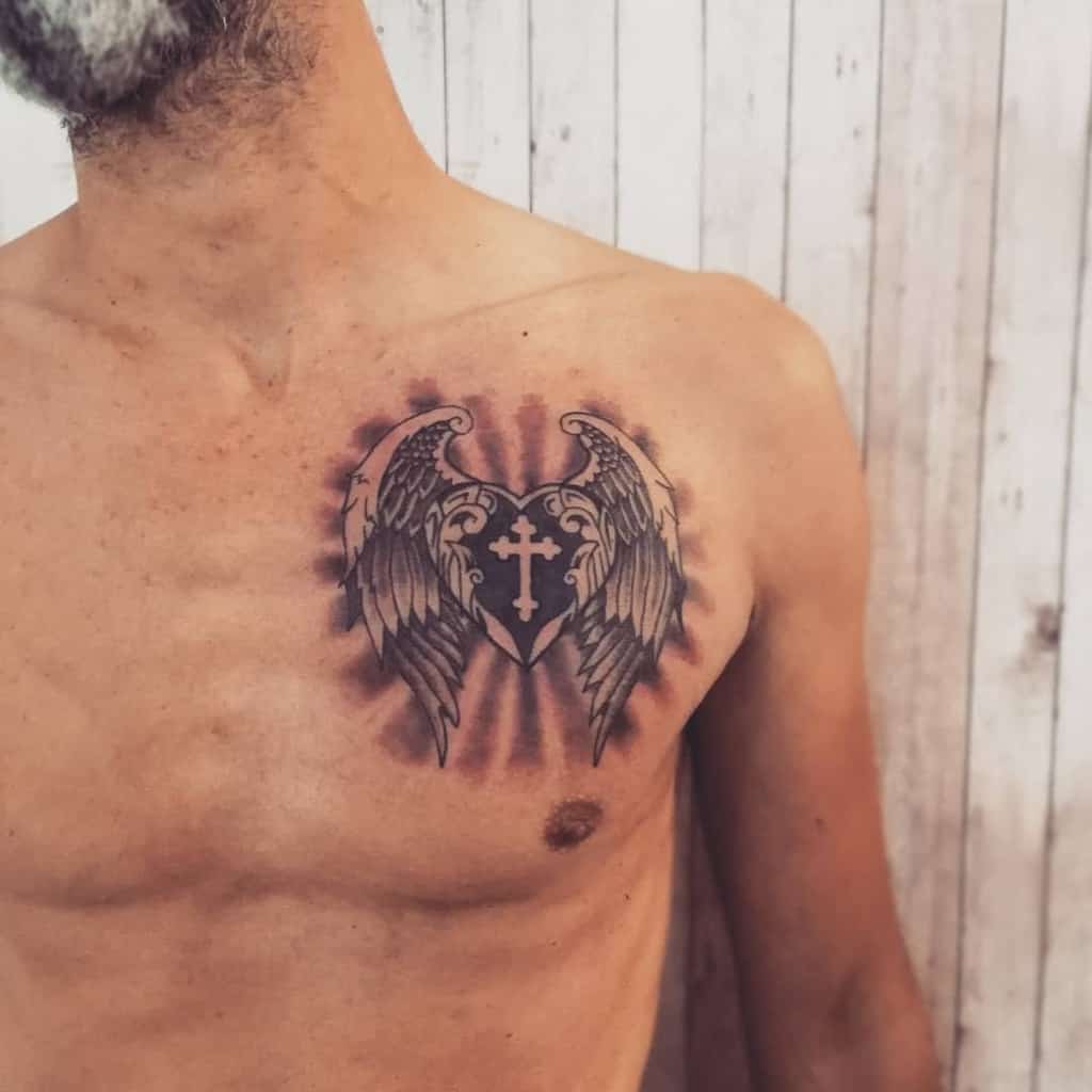 A shirtless person featuring a chest tattoo with heart wings surrounding a cross