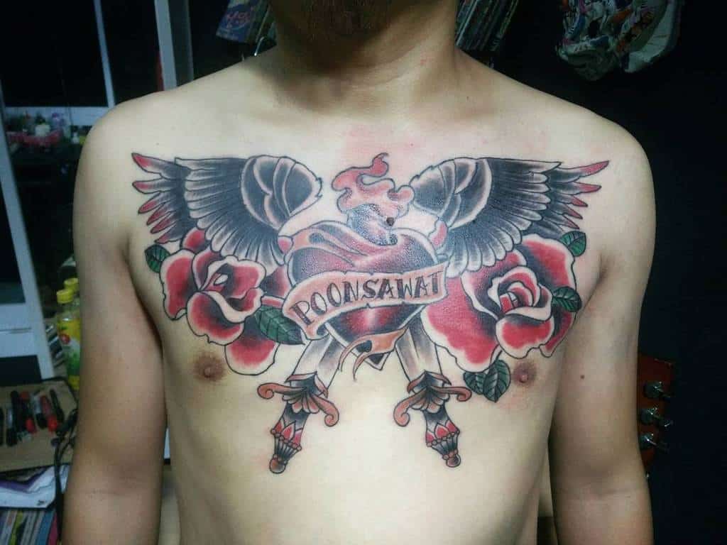 Chest tattoo with a heart, roses, angel wings, and a "Poonsawat" banner, intricately done in red, black, and grey