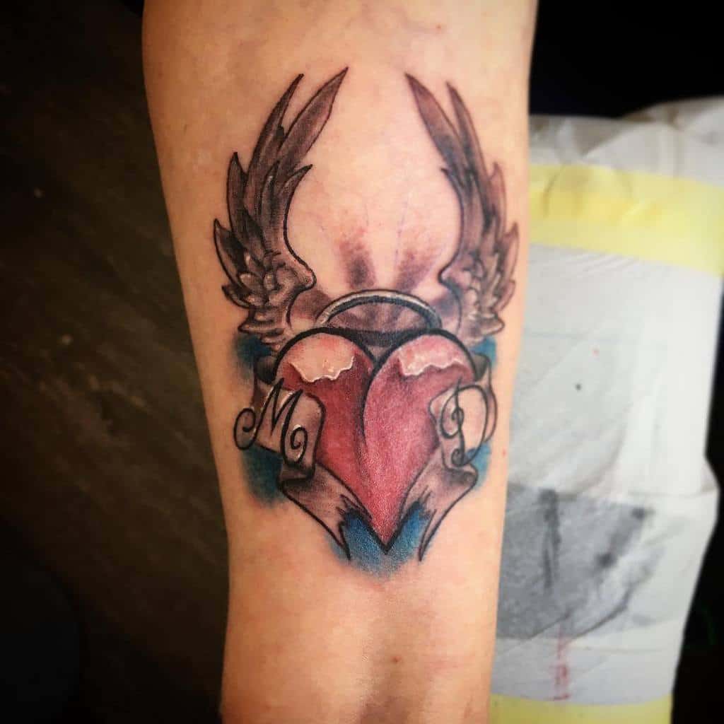 Tattoo of a heart with wings and the initials "M" and "D" on the inner forearm