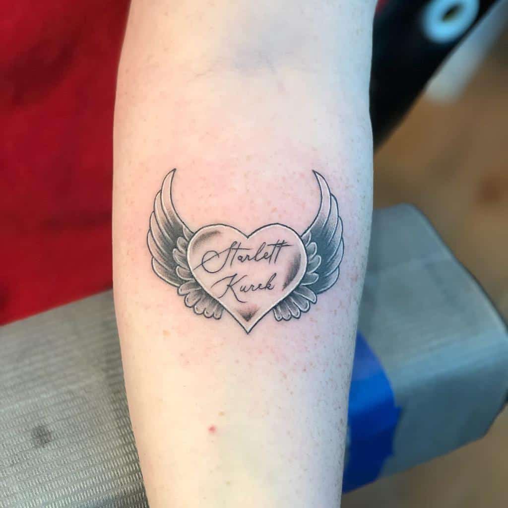 Black and grey tattoo of a heart with angel wings, featuring the name 'Starlett Kurek' in elegant script