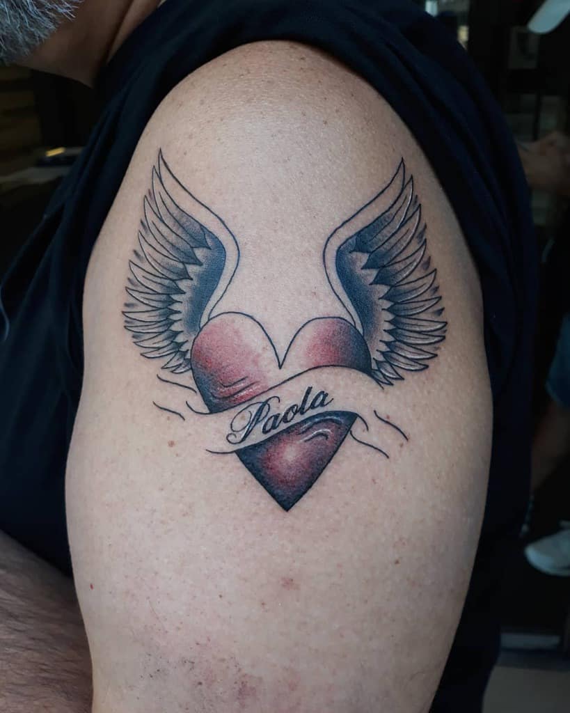 A heart tattoo with wings on an arm, featuring the name "Paola" elegantly scripted across it