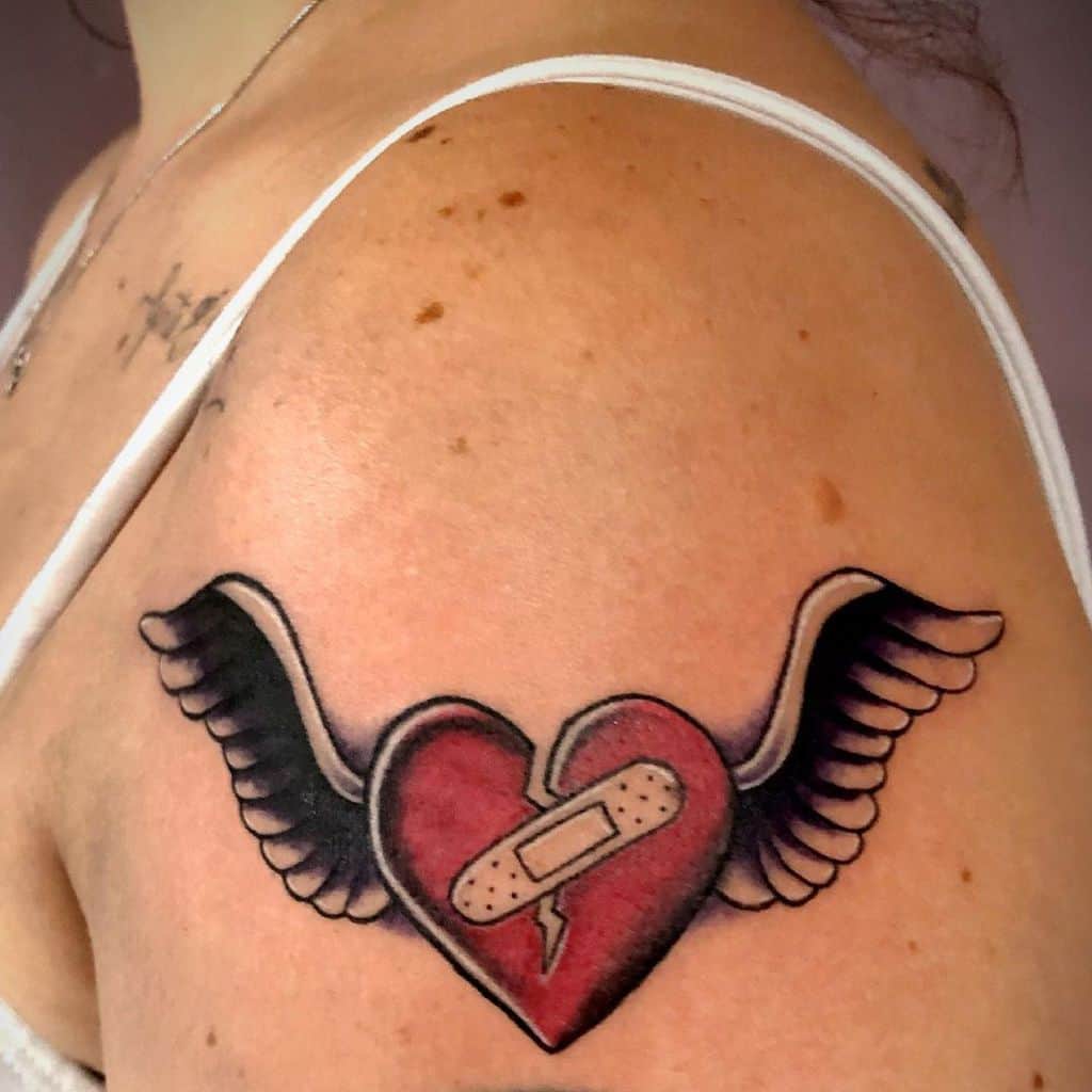 Tattoo of a heart adorned with wings and a bandage