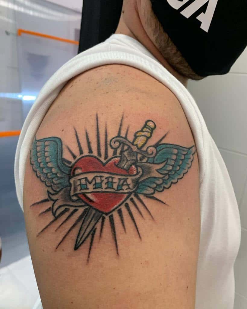 Tattoo of a heart with wings enveloping a dagger on an arm, with "MAMA" elegantly inscribed inside the heart