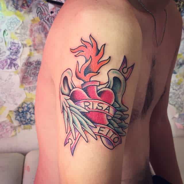 Tattoo of a flaming heart with radiant wings on a person's upper arm, featuring the words "RISA" and "EITO"