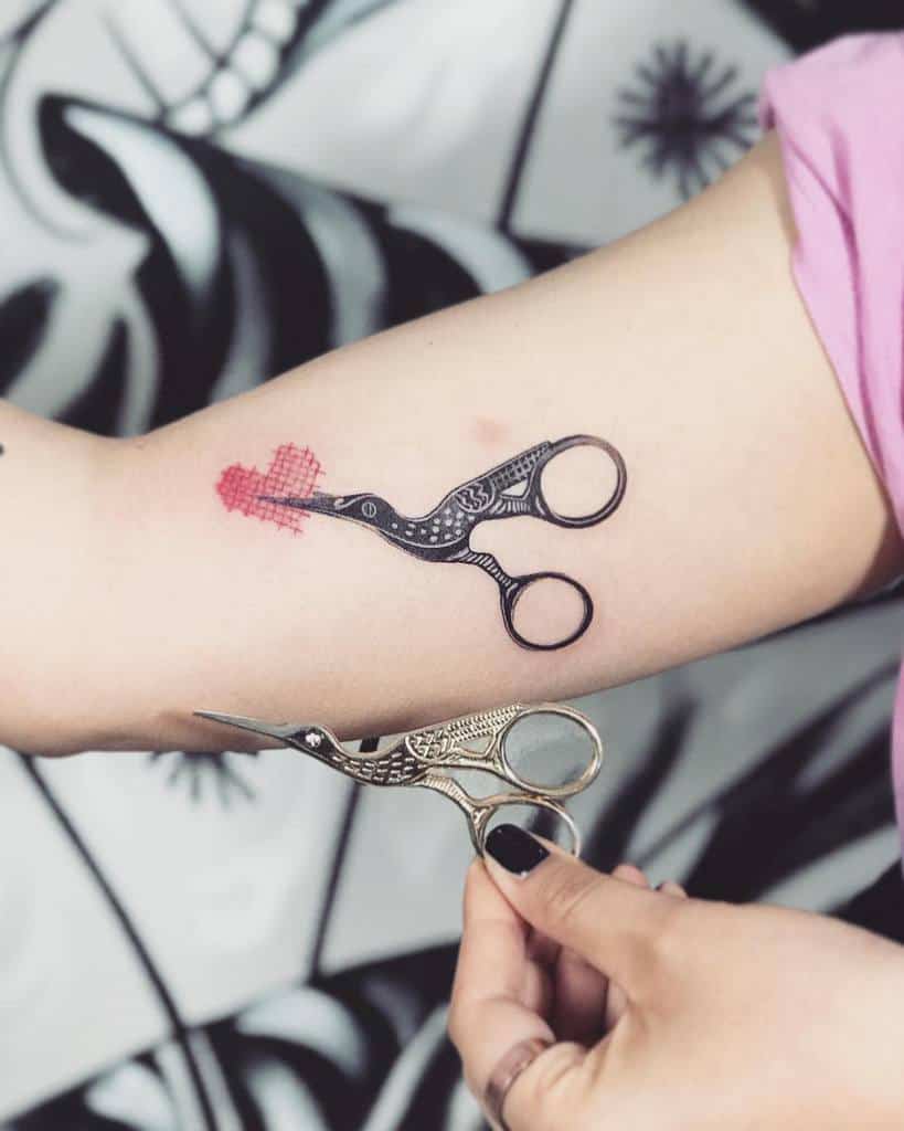 Creative tattoo of vintage embroidery scissors forming a cross-stitched red heart, designed to resemble real scissors