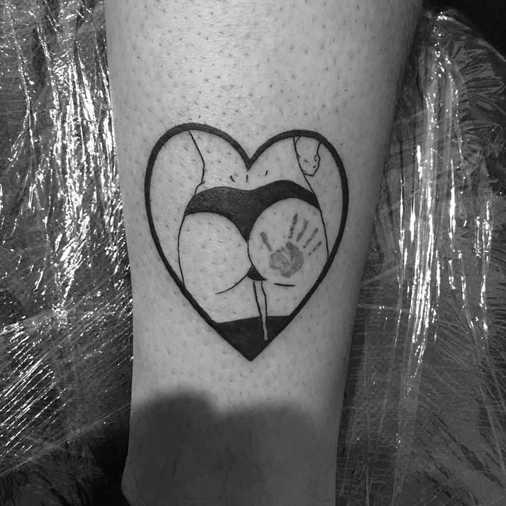 Black and grey heart-shaped tattoo with an artistic depiction of a woman's lower back and hips, with a handprint on the skin.