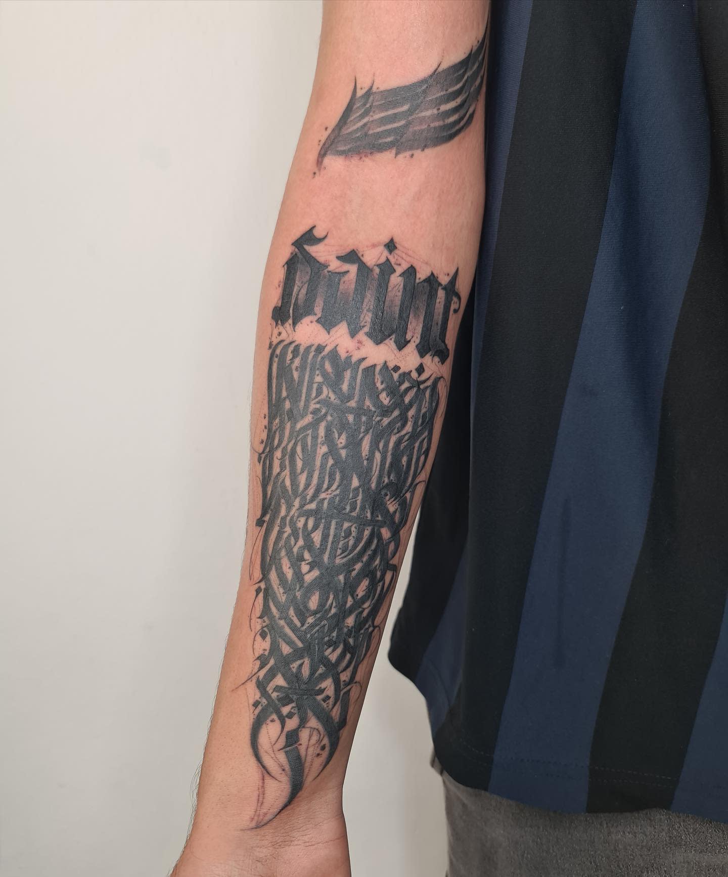 Tattooed forearm featuring "Saint" text and detailed black ink design underneath