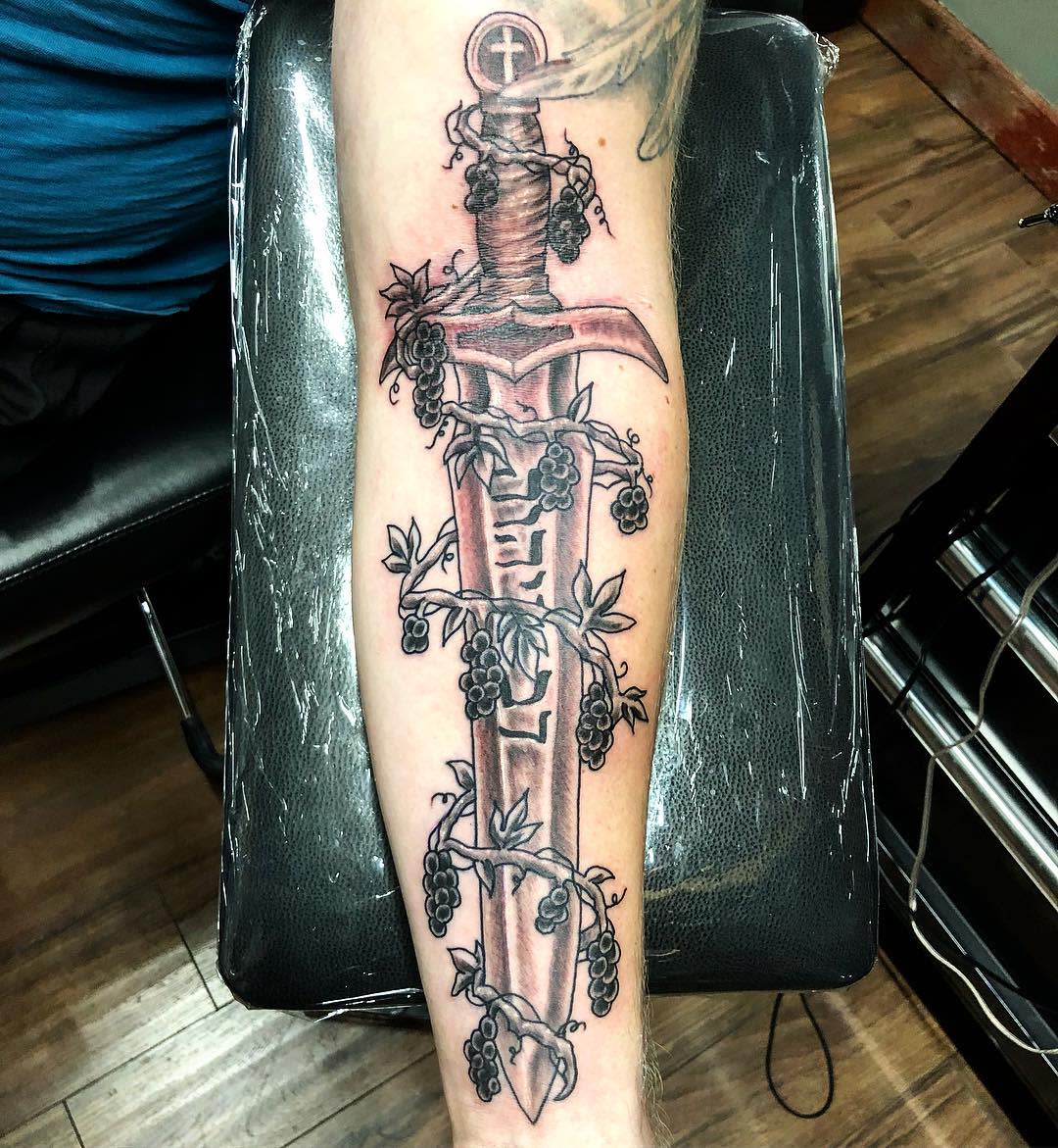Forearm tattoo of a sword with vines and berries wrapped around it