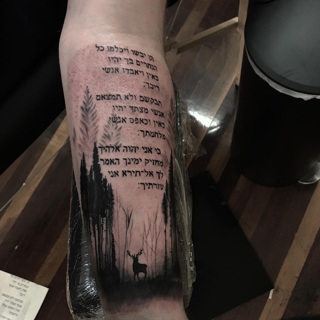 Tattoo of Hebrew text above a forest scene with a deer on a forearm