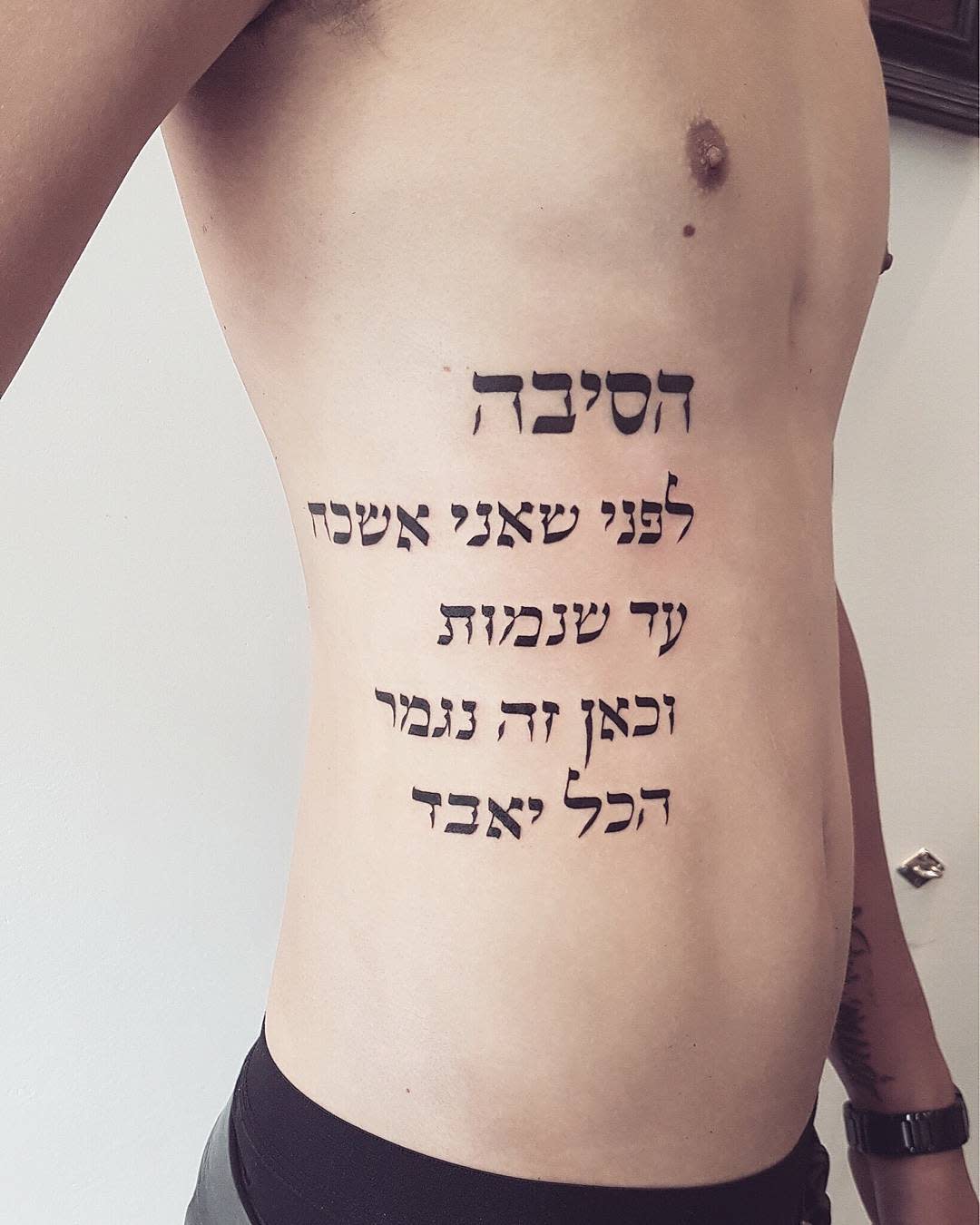 Side of torso with dark text tattoo written in Hebrew