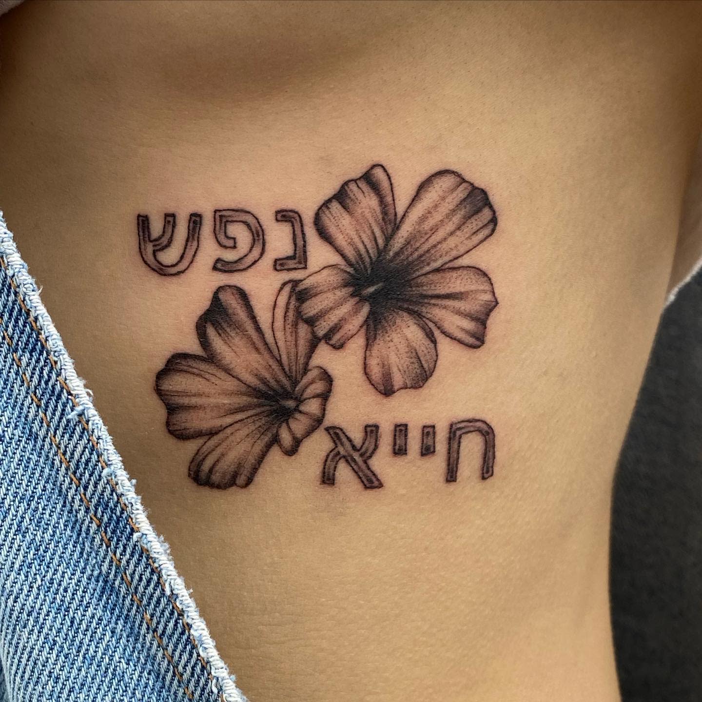 Tattoo of two flowers and Hebrew text on a side